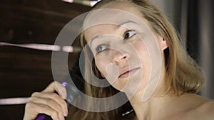 Young woman in towel combing her hair with hot comb in front of a mirror. Skin care and home Spa