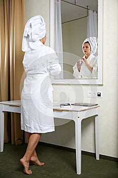 Beautiful young woman look in mirror applying cream, pretty lady wrap towel on head put facial moisturizer lifting