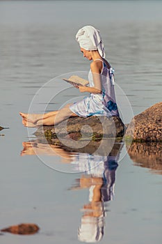 Young woman with a towel on her head at the sea. Lady reads a book in the water. The concept of summer outdoor recreation, relaxat
