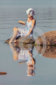 Young woman with a towel on her head at the sea. Lady reads a book in the water. The concept of summer outdoor recreation, relaxat