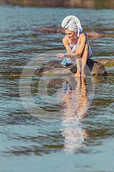 Young woman with a towel on her head at the sea. The lady touches the water with her hands. The concept of summer outdoor recreati