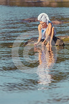 Young woman with a towel on her head at the sea. The lady touches the water with her hands. The concept of summer outdoor recreati