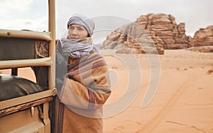 Young woman in traditional Bedouin coat - bisht - and headscarf, posing next to old truck rear frame, looking away - desert photo