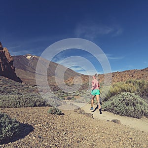 Young woman trail running in mountains on sunny day