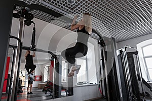 Young woman trainer in sportswear with a slim body doing exercises for hands indoors. Girl performs physical exertion in training