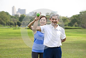 young woman trainer is teaching a senior man to use dumbbell while exercise rehabilitation in the park