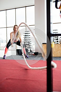Young Woman training with battle rope in cross fit gym