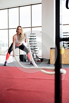 Young Woman training with battle rope in cross fit gym