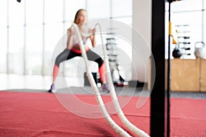 Young Woman training with battle rope in cross fit gym