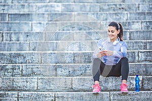 Young woman after training checks sport tracker. Fitness concept outfit thermal underwear headphones and smartphone