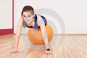 Young woman is training by doing push up with exercise ball in gym