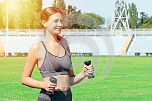 Young woman is training with dumbbells at the stadium. Strong muscles and active sport concept