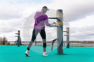 Young woman training in fighting sport alone on the sports ground with traditional dummies