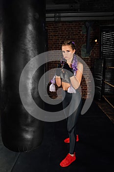 Young woman trains in boxing ring with heavy punching bag.