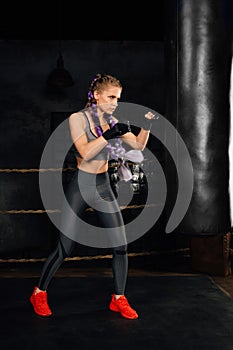 Young woman trains in boxing ring with heavy punching bag.