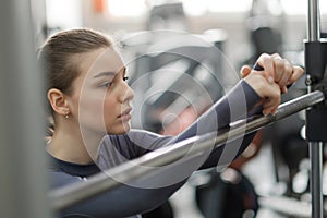 A young woman trains in the gym. Tired face, hands resting on the barbell.