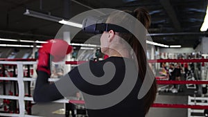 A young woman trains her punches wearing VR glasses in the gym - shadow boxing