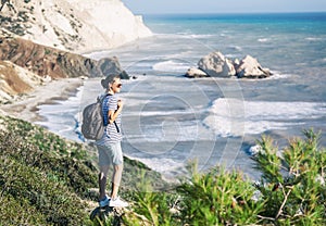 young woman travel girl with backpack walks on beautiful landscape background, sea and hills, cape of Aphrodite, Cyprus, popular