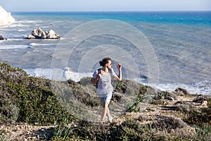 young woman travel girl with backpack walks on beautiful landscape background, sea and hills, cape of Aphrodite, Cyprus, popular
