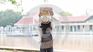 Young woman traveler with backpack and hat looking the map with temple Thailand background