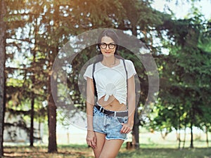 Young woman traveler with backpack standing alone in forest. Hipster girl in sunny woods