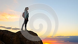 Young Woman Traveler with Backpack Standing on the Top of the Rock at Summer Sunset. Travel and Adventure Concept.