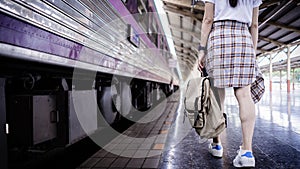 Young woman traveler with backpack walking at train station and waits train on railway platform. Travel concept