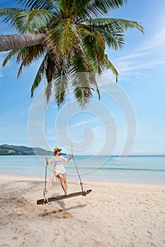 Young woman traveler enjoying on the swing at beautiful tropical white sand beach, Summer vacation and Travel concept