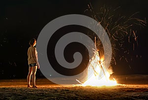 Young woman traveler feeling heat of beach bonfire with sparks