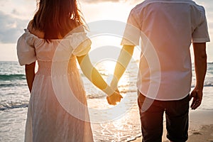 Young woman traveler holding man`s hand and looking beautiful sunset on the beach, Couple on vacation in summer concept