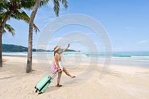 Young woman traveler with luggage relaxing and enjoying at beautiful tropical sand beach, Summer vacation and Travel concept