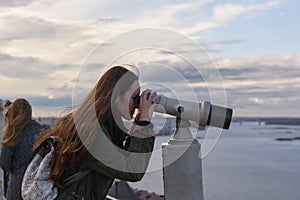 A young woman traveler on the observation deck looking through binoculars at the panorama of the city of Nizhny Novgorod