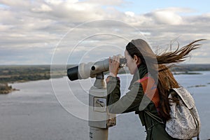 A young woman traveler on the observation deck looking through binoculars at the panorama of the city of Nizhny Novgorod