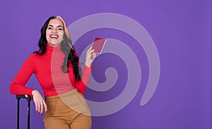 Young woman traveler with passport and suitcase against purple background