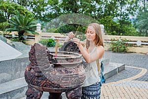 Young woman Traveler praying in polite action with incense sticks at buddhism temple in Vietnam