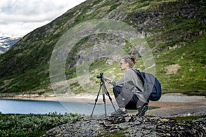 Young woman traveler professional photographer takes a picture of the landscape on the camera on a tripod, Norway, beautiful