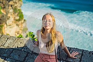 Young woman traveler in Pura Luhur Uluwatu temple, Bali, Indonesia. Amazing landscape - cliff with blue sky and sea