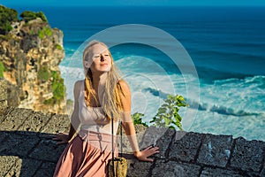 Young woman traveler in Pura Luhur Uluwatu temple, Bali, Indonesia. Amazing landscape - cliff with blue sky and sea
