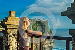 Young woman traveler in Pura Luhur Uluwatu temple, Bali, Indonesia. Amazing landscape - cliff with blue sky and sea