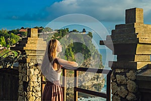 Young woman traveler in Pura Luhur Uluwatu temple, Bali, Indonesia. Amazing landscape - cliff with blue sky and sea