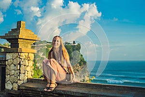 Young woman traveler in Pura Luhur Uluwatu temple, Bali, Indonesia. Amazing landscape - cliff with blue sky and sea