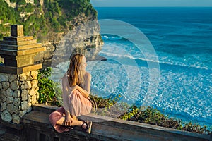 Young woman traveler in Pura Luhur Uluwatu temple, Bali, Indonesia. Amazing landscape - cliff with blue sky and sea