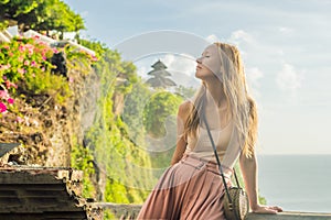 Young woman traveler in Pura Luhur Uluwatu temple, Bali, Indonesia. Amazing landscape - cliff with blue sky and sea