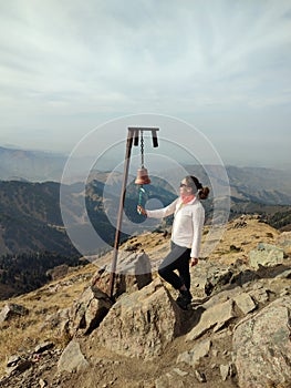 Young woman traveler rings bell at mountaintop