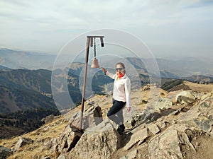 Young woman traveler rings bell at mountaintop