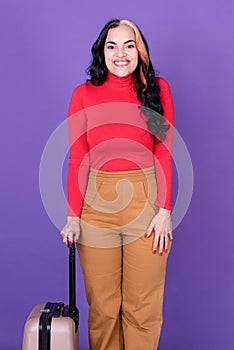 Young woman traveler with suitcase against purple background
