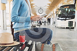 Young woman traveler waiting for a bus on a bus station and using digital tablet, travel and active lifestyle concept