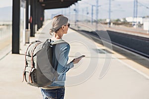 Young woman traveler waiting for a train on a railroad station, travel and active lifestyle concept