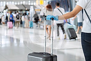 Young woman traveler wearing nitrile glove holding handle luggage in airport terminal, protection Coronavirus disease Covid-19