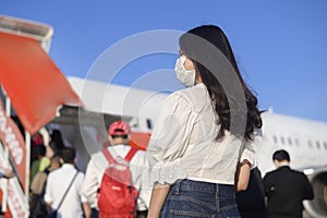 Young woman traveler wearing protective mask getting in airplane and ready to take off, travel under Covid-19 pandemic, safety